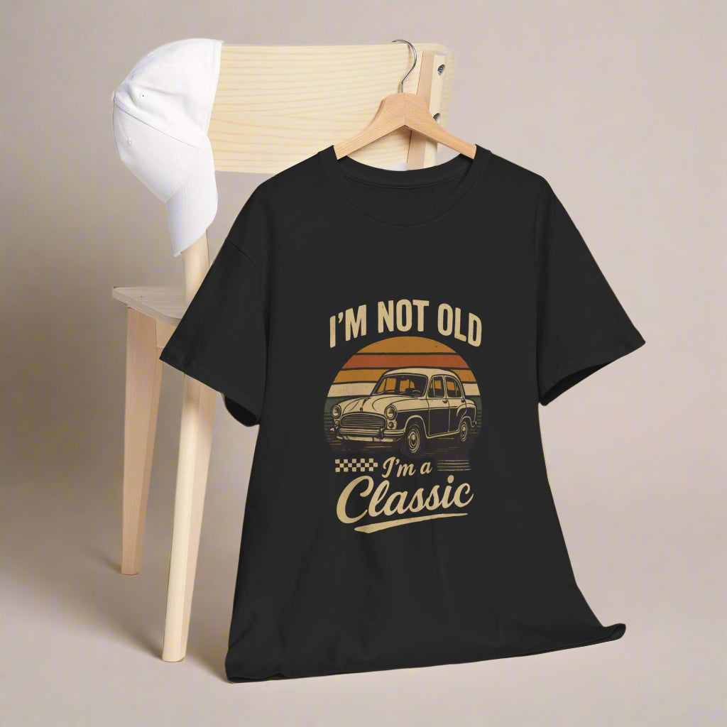 Black t-shirt with vintage car graphic and text 'I'm not old, I'm a classic' on a wooden chair.
